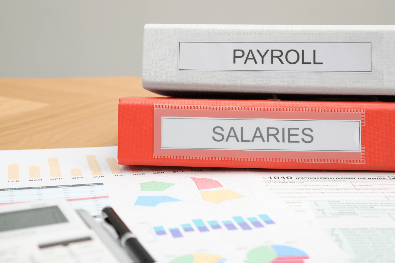 Payroll folders, charts, and calculator on desk, illustrating the benefits of outsourcing payroll for accuracy and organization.